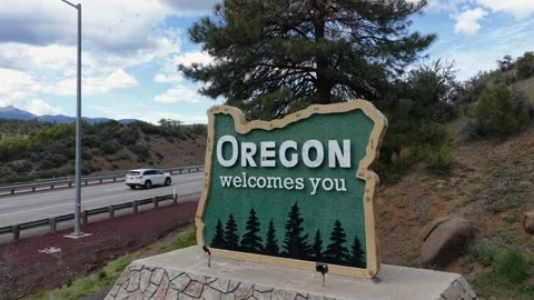 Oregon Welcomes You state border sign on stone base stands beside highway with Stock Footage 337529068