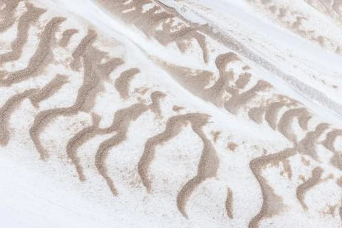 Organic, abstract patterns of sand swept across white snow Stock Photos