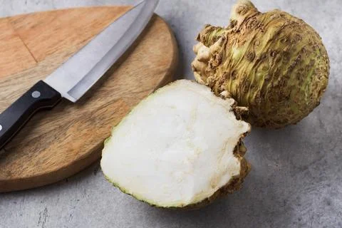 Organic celery root, half and whole, next to wooden board and knife on gray.. Stock Photos