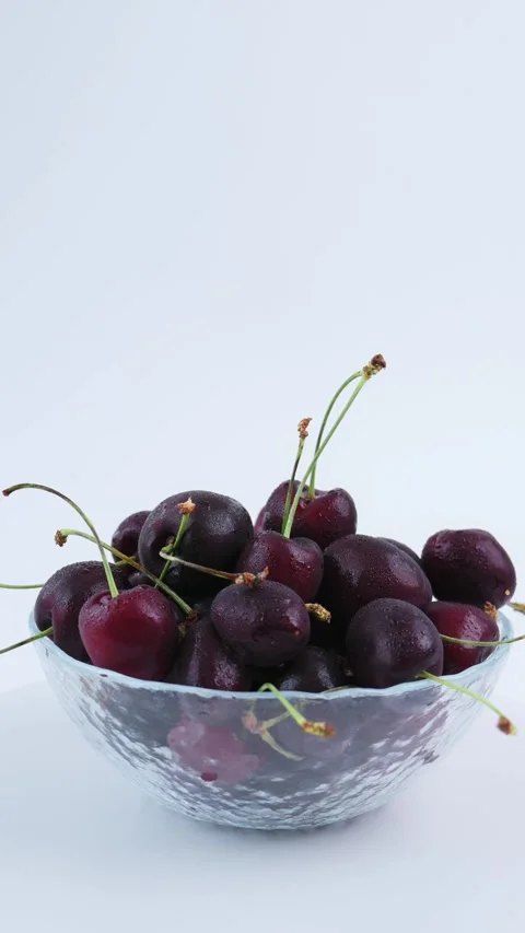 Organic dark cherry arranged in transparent glass bowl with clean white backdrop Video stock 342964186