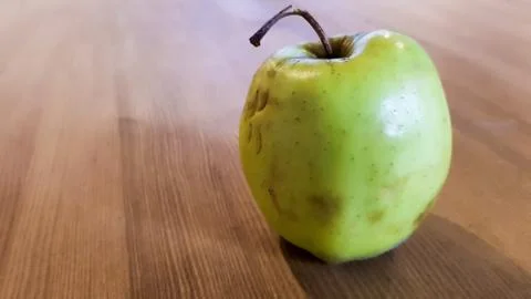 Organic juicy bio apple ugly, with defects of edible lies on a wooden table. Stock Photos