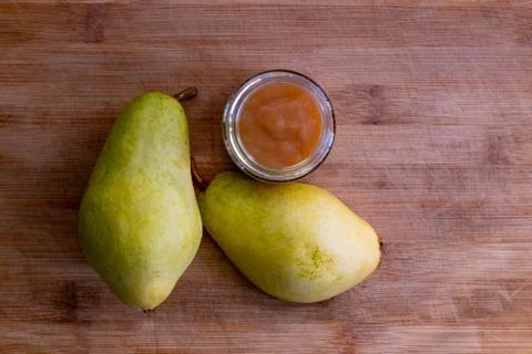 Organic pureed pear in a glass jar with whole pear on a bamboo board Stock Photos