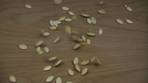 Organic roasted pumpkin seeds falling on wooden background. Slow motion. Stock Footage 130918425