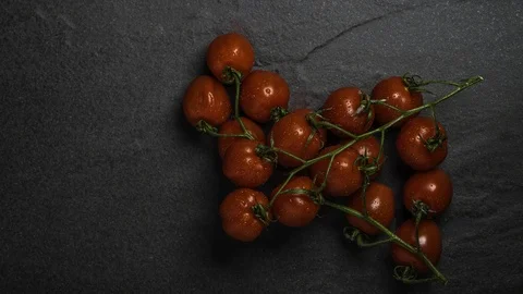 Organic Roma Vine Cherry Tomatoes on a black stone background Vídeos de archivo 106027619