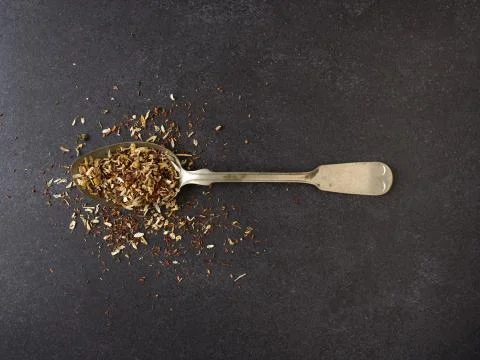 Organic tea blend on a rustic spoon, dark stone background Stock Photos