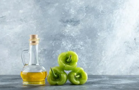 Organic vegetables. Stack of sweet peppers with bottle of oil on grey background Stockfoto's