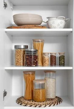 Organized kitchen pantry with various dry goods in glass jars and kitchenware Stock Photos