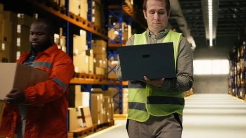 Organizing cargo parcel, man worker with laptop, in distribution center facility Stock Photos