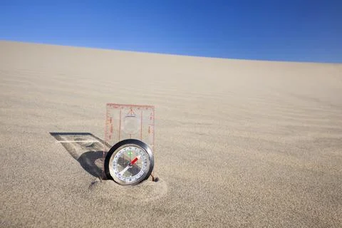 Orienteering compass placed upright in a sand dune beneath a clear blue sky.. Stock Photos