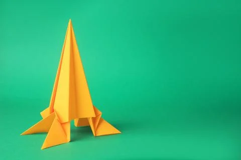 Origami art. Handmade yellow paper rocket on green background, space for text Stock Photos