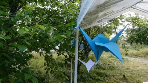 Origami crane hanging on a thread. Decorating a tent in nature. Stock Photos
