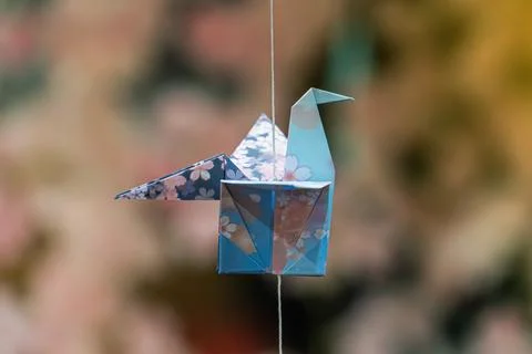 Origami crane suspended by thin string, intricate floral pattern paper, natur Stock Photos