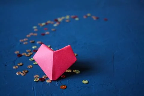 Origami paper heart made of red paper on a dark blue background with sequins. Stock Photos
