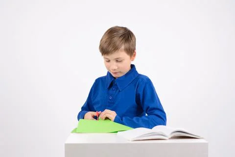 Origami: studious boy with scissors is studying the book to make Stock Photos