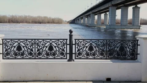 Ornate black iron railing on river embankment with bridge behind Stock Footage 332432831