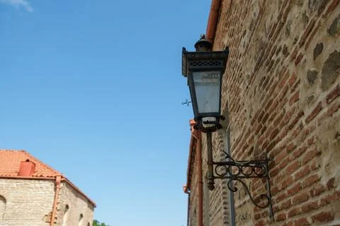 Ornate black wall lantern mounted on weathered brick and stone building beneath Stock Photos