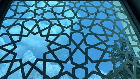Ornate geometric metalwork frames a bright blue sky with soft white clouds, c Foto stock