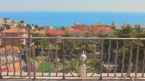 Ornate railing frames red roofed homes, garden palms and blue sea in Imperia Stockbeeldmateriaal 348391901
