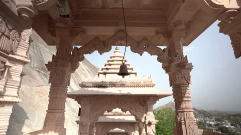 Ornate temple structure with central bell, stone columns, and mountain backdrop Stock Footage 314004324