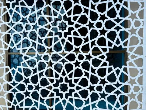 Ornate white star pattern creates a geometric lattice over window reflecting  스톡 사진