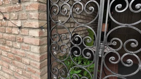 Ornate wrought iron gate with brick wall and potted plants, elegant entryway Stock Footage 339030163