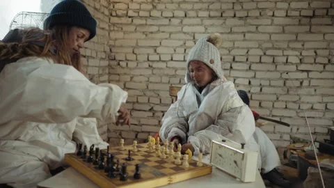 Orphans Play Chess in Cold Room While Someone Sharpens Wood Behind Video stock 327019701