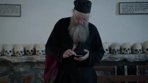 Orthodox monk using smartphone inside an ossuary Stock Footage 330196271