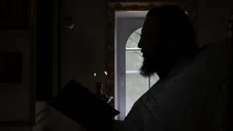Orthodox priest in backlight opposite the window praying in church Stock Footage