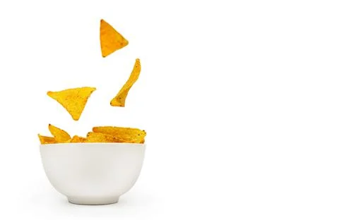 Ortilla corn chips are falling into a white ceramic bowl. Stock Photos