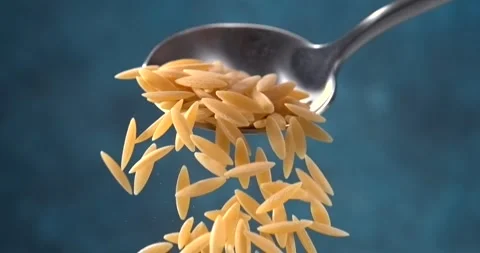 Orzo pasta falling from a spoon in slow motion on blue background Stock Footage 346322397