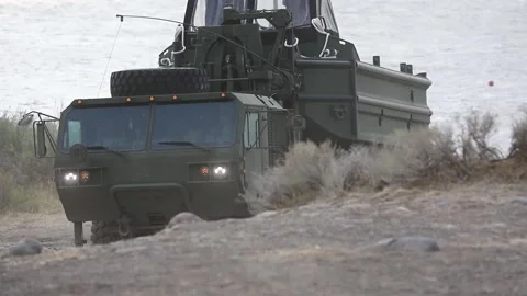 Oshkosh reversing towards river to release amphibious boat Stock Footage 160106757