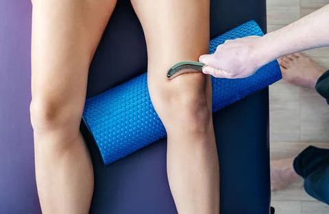 Osteopath performing IASTM technique to fix knee cap Patellofemoral pain Stock Photos