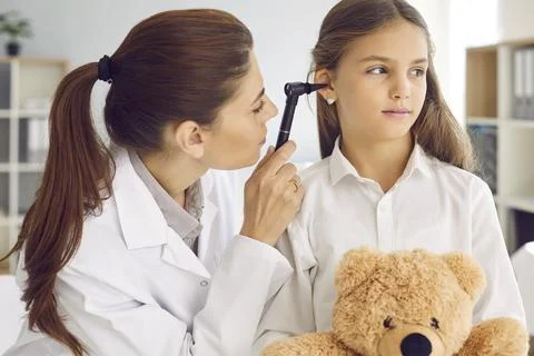 Otolaryngologist examining child's ear with otoscope during checkup at her Stock Photos