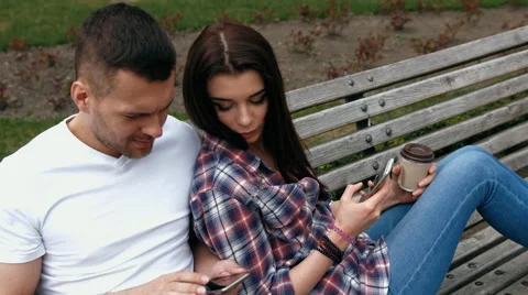Ouple sitting on a bench using mobile phone or digital tablet Stock Footage 62630572