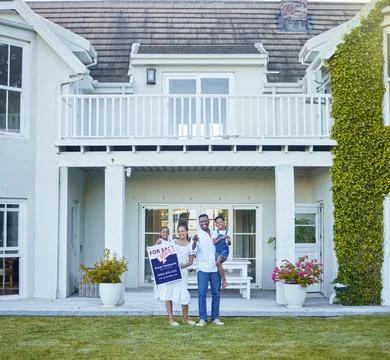 This is our new home. a young family posing in front of a house with a sold sign Stock Photos
