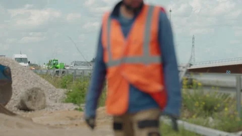 Out of focus construction worker in a high visibility vest walking along a Stock Footage 334044600