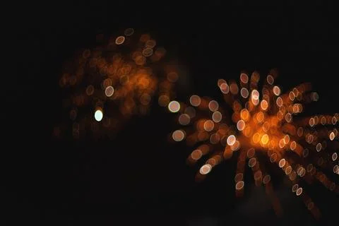 Out of focus golden fireworks exploding and glowing brightly against a dark.. Stock Photos