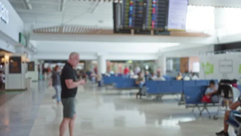 Out-of-focus man walks through busy airport terminal with seating area and .. Vidéo 309134555