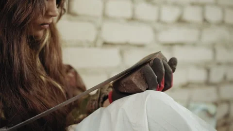 Outcast Child Sharpens Blade on Stone in Gritty Shelter Video stock 329463806