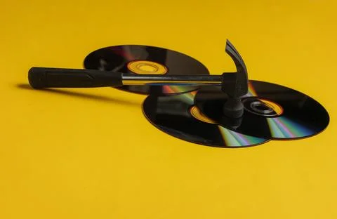 Outdated storage media. Hammer with CD discs on a yellow background 写真素材