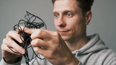 Outdated technology. Frustrated man struggles to untangle wired lapel microphone Stock Footage 312099096