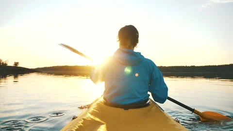 Outdoor activities, man is kayaking on calm lake against sunset rays Stock Footage