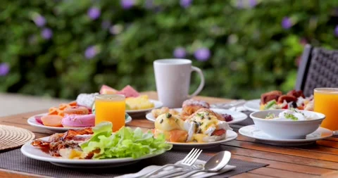 Outdoor breakfast on table with eggs Benedict, salad, donuts, coffee, Stock Footage 312002134