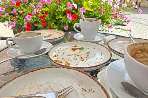 Outdoor cafe setting featuring a glass table with empty coffee cups and plate Stock Photos