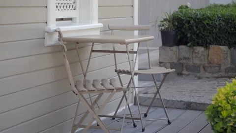 Outdoor cafe table and chairs on patio with green foliage and stone wall. Vídeos de archivo 332579088