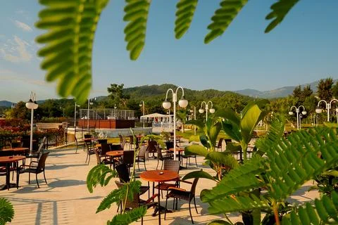 An outdoor dining area with empty tables and chairs. Sunlight shines on green Stock Photos