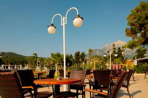 An outdoor dining area with empty tables and chairs. Sunlight shines on green Stock Photos