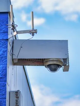 Outdoor dome security camera mounted on building wall against blue sky Stockfoto's