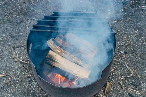 Outdoor fire pit ablaze, logs crackling, with smoky tendrils in open air. Stock Photos