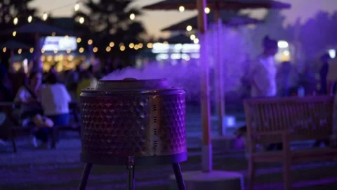 Outdoor fire pit burning softly near festival crowd, purple night tones and Stock Footage 321817963